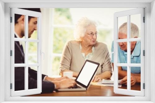 Businessman using laptop while senior couple is reading document