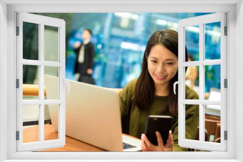 Woman use of cellphone with notebook computer at coffee shop