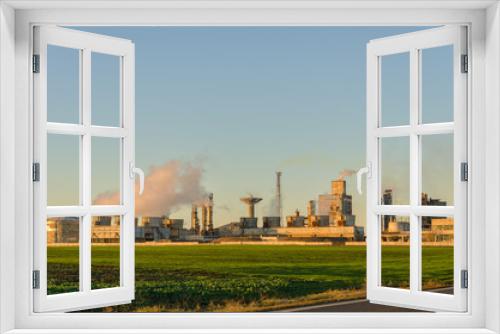 Fototapeta Naklejka Na Ścianę Okno 3D - Chemical plant with smoke in sunset light on a green field against clear sky