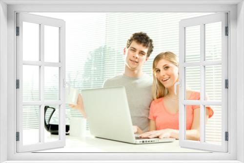 Young casual couple have breakfast with coffee and laptop with venetian blind window background