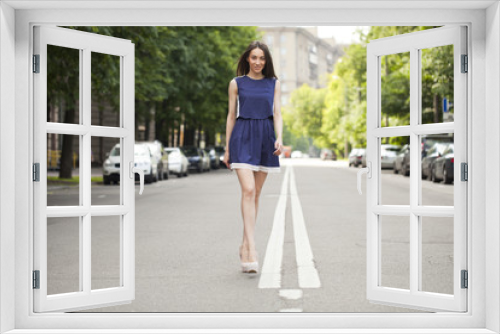 Young beautiful woman in a blue short dress walking on the road