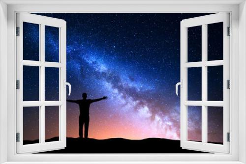 Fototapeta Naklejka Na Ścianę Okno 3D - Night landscape with Milky Way. Silhouette of a standing young man with raised up arms on the mountain. Beautiful Universe. Travel background with blue night starry sky