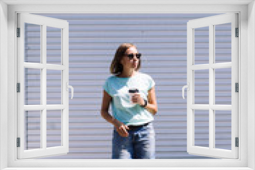 Portrait of young woman in sunglasses and casual clothes with cup of coffee to go looking pensively away on white background.