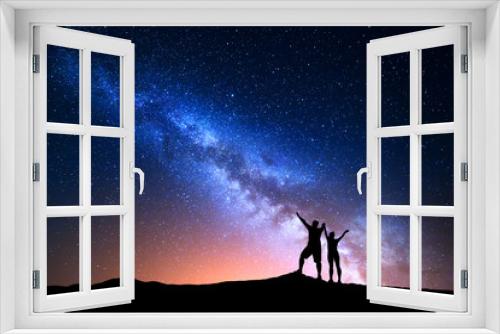 Fototapeta Naklejka Na Ścianę Okno 3D - Milky Way. Colorful night sky with stars and silhouette of standing happy man and woman with raised  up arms on the hill. Blue milky way with people on the mountain. Background with beautiful universe