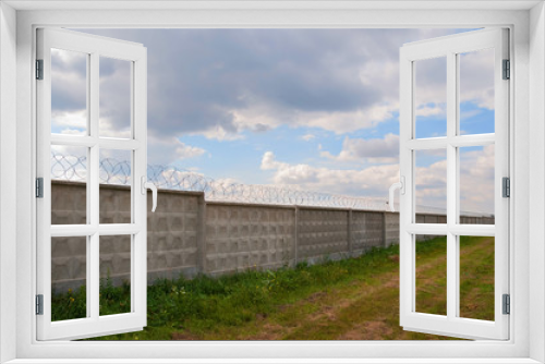 Fototapeta Naklejka Na Ścianę Okno 3D - Wall with barbed wire on a background of blue sky. long fence