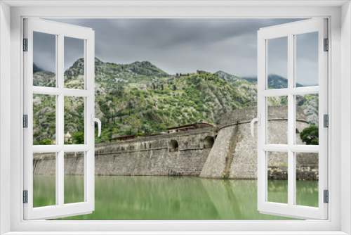 Fototapeta Naklejka Na Ścianę Okno 3D - Kampana Tower and Citadel, the World Heritage listed fortifications surrounding the medieval village of Kotor in Montenegro reflected in the Skurda River, with mountains in the background.