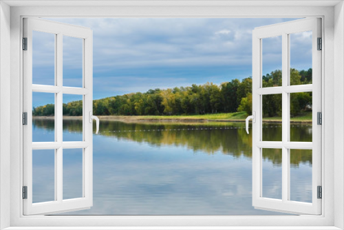 Fototapeta Naklejka Na Ścianę Okno 3D - Green leaves on the trees in autumn. Blue sky reflected in a calm lake. Crystal Forest reflection in the lake