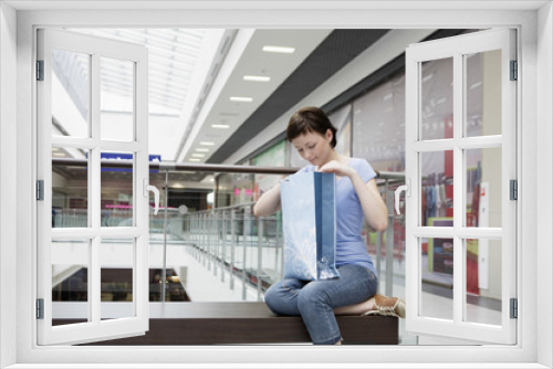 Young woman looking in shopping bag while sitting at mall