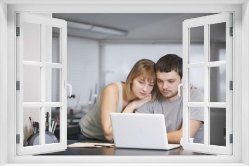 Young couple using laptop together at kitchen counter