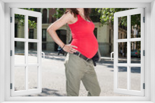 portrait of brunette brown hair pregnant woman with red shirt green trousers and black sunglasses in summer in Madrid urban street
