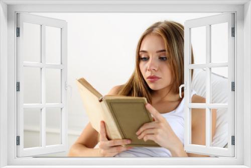 Young beautiful blonde woman lying in bed reading old book