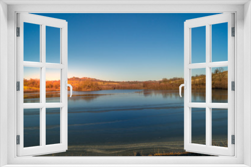 Fototapeta Naklejka Na Ścianę Okno 3D - expanse of green grass on the lake with blue sky, countryside and farm around the lake, sunlit water