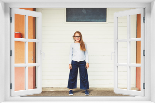 Outdoor funny portrait of a cute little 9-10 year old girl wearing blue top, denim culottes and eyeglasses