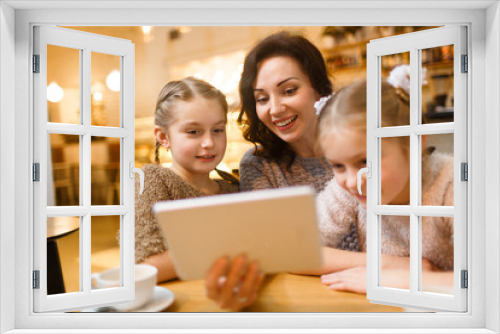 Happy young woman with touchpad showing her twin daughters movie for children