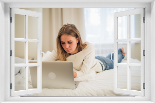 A cute young woman smiling excitedly at her laptop screen. She is relaxing in bed.