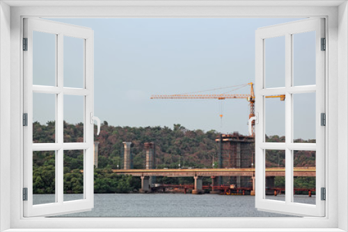 Fototapeta Naklejka Na Ścianę Okno 3D - Construction of tall concrete piers using tower crane for new bridge across Mandovi River in Goa, India