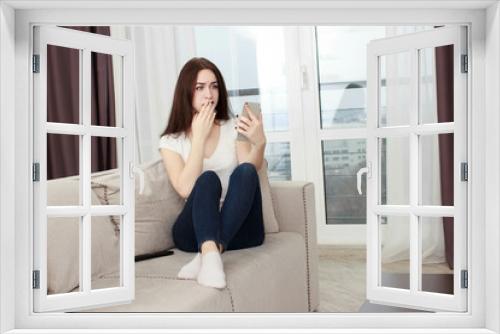 Happy girl reading a message in a smart phone sitting on a couch at home.