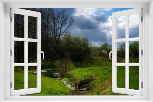 Fototapeta Naklejka Na Ścianę Okno 3D - Idyllic brook flowing through a green meadow with trees and shrubs, blue sky with clouds in spring, rural natural landscape