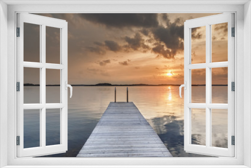 Fototapeta Naklejka Na Ścianę Okno 3D - Beautiful glowing orange sunset over a rustic timber plank jetty reflected in the mirror calm waters of the sea below, a background of natural beauty and serenity. Northern sea, Sweden, Scandinavia.