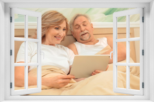 Elderly couple resting in bed with tablet computer