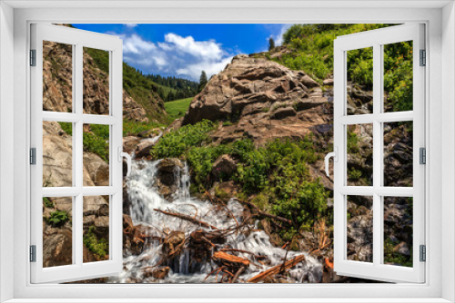 Fototapeta Naklejka Na Ścianę Okno 3D - Waterfall in the rocks against the backdrop of mountains and sky with clouds