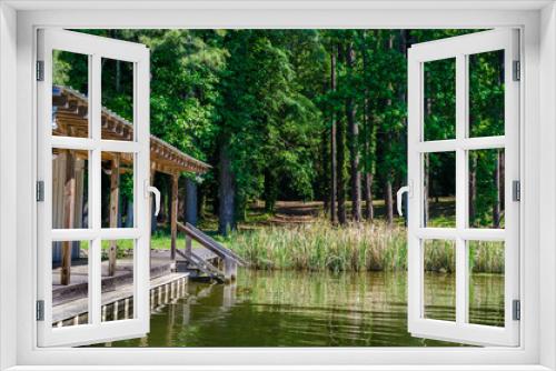 Fototapeta Naklejka Na Ścianę Okno 3D - Lake boat house resting on reflective lake shoreline water.  Relaxing tranquil outdoor scene of woods, grass and water with boat house.  
