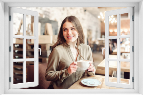 Pretty girl using cell phone smiles and looks over her shoulder out of frame.In caffe.