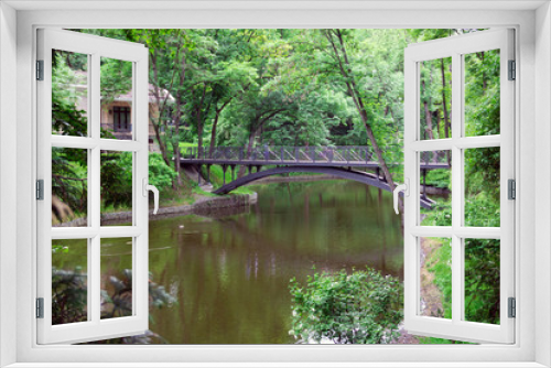 Fototapeta Naklejka Na Ścianę Okno 3D - Metal bridge over a lake in a green garden