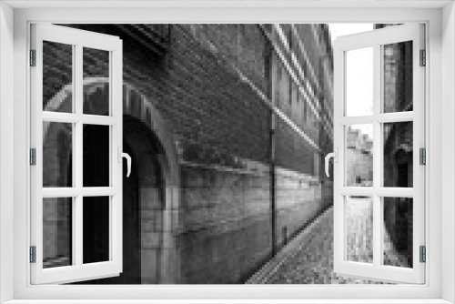 Fototapeta Naklejka Na Ścianę Okno 3D - View along narrow street of buildings and cobbles, black and white, Belgium.