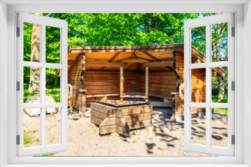 Fototapeta Naklejka Na Ścianę Okno 3D - Wooden hiking shelter with lifeboat to the side and a fire pit for cooking and warmth in front. Forest in background.