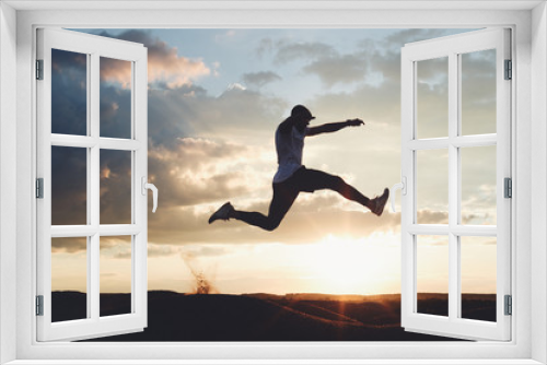 Fototapeta Naklejka Na Ścianę Okno 3D - Silhouette of a strong athlete jumping over the hills. Man at sunset in nature is engaged in fitness. Intentional dark colors