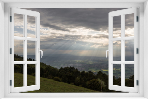 Fototapeta Naklejka Na Ścianę Okno 3D - View of a valley from a mountain, with sun rays coming out through the clouds and lighting up some areas of the ground 