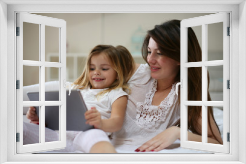 Happy young mother with daughter using digital tablet on bed at home.