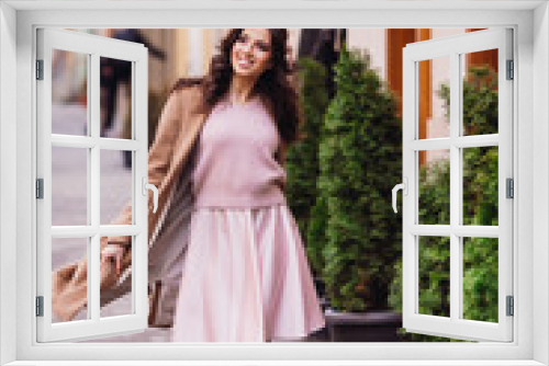 Woman in pink dress and beige coat walks along old street