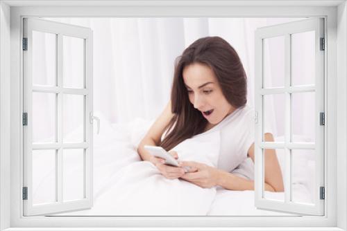 Young happy beautiful brunette woman using the mobile phone in white bed.