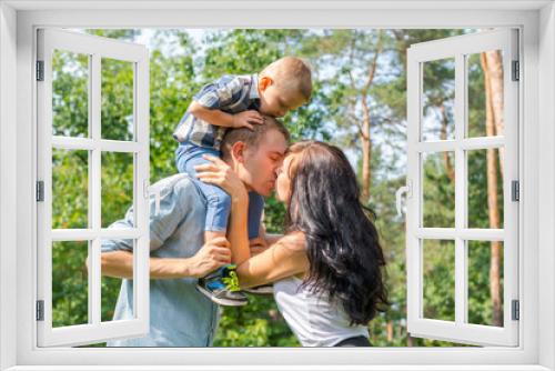 Mom kisses daddy who keeps their child on their shoulders