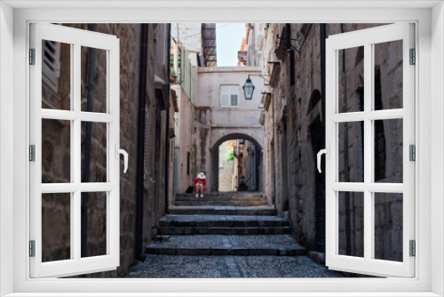 Fototapeta Naklejka Na Ścianę Okno 3D - Narrow steep street of beautiful ancient european village or city, Dubrovnik Croatia with cobbled paved walls and floors. Lonely lost tourist sits on steps, exploring