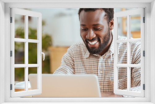 Pleasant cheerful man smiling while working on laptop