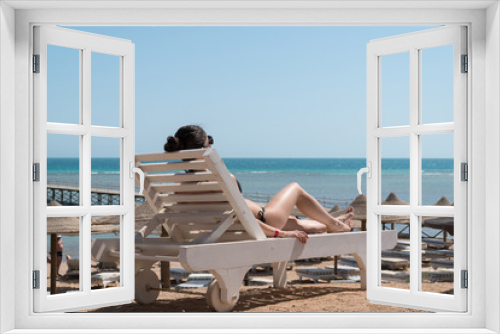 Fototapeta Naklejka Na Ścianę Okno 3D - Girl sunbathing on a lounger on the beach. In the background a pier is visible