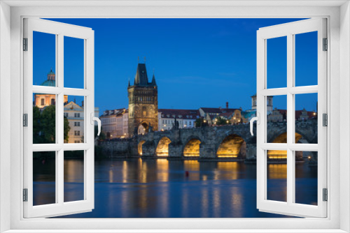 Lit Charles Bridge (Karluv most) and old buildings at the Old Town and their reflections on the Vltava River in Prague, Czech Republic, at dusk.
