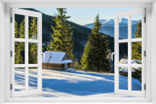 Fototapeta Naklejka Na Ścianę Okno 3D - Wooden cottage in the mountains. The fir trees are covered with morning rays. Shadows from the trees on the snow. Winter in Ukrainian Carpathian Mountains.