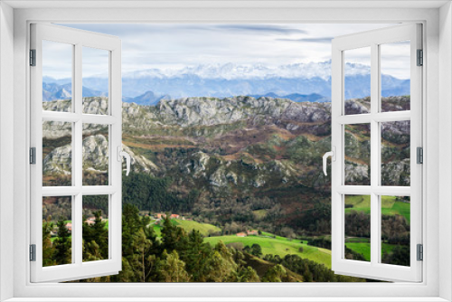 Picos de Europa Mountain Range landscape with a green field in the front and mountains covered by snow at the end