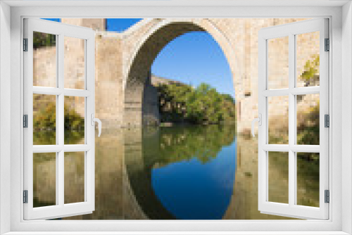 arch of Alcantara bridge, landmark and monument from ancient Roman age, reflected on water of river Tagus, Tajo in Spanish, in Toledo city, Spain, Europe
