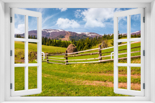 Fototapeta Naklejka Na Ścianę Okno 3D - wooden fence along the dirt road on grassy hills of Carpathian alps. gorgeous springtime countryside with spruce forest and mountain ridge with snowy tops in the distance. 