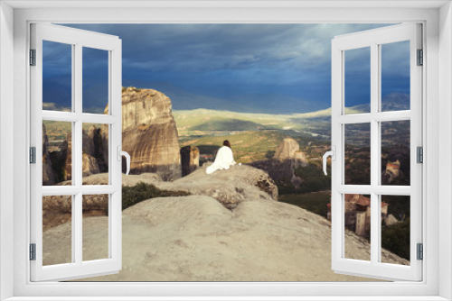 Fototapeta Naklejka Na Ścianę Okno 3D - Alone female with cap in the white plaid on the edge of the rock look on the monasteries of Meteora. Female on the rock and monasteries of Meteora in Greece in Thessaly at the early morning