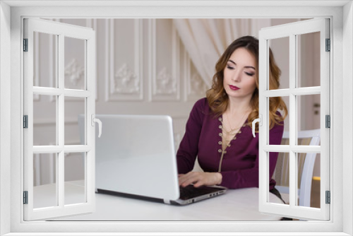 Beautiful woman is sitting in an expensive kitchen behind a laptop. Work at home, realtor, online store.