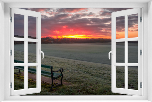 Fototapeta Naklejka Na Ścianę Okno 3D - A beautiful early morning sunrise over an open frosty field parkland with an empty bench seat in the foreground