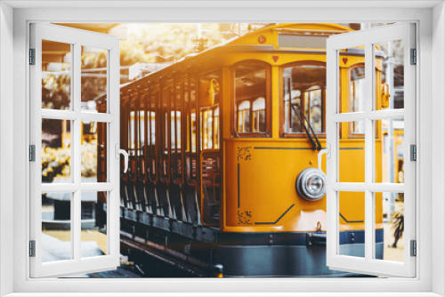 Fototapeta Naklejka Na Ścianę Okno 3D - View of empty yellow glossy excursion tram waiting at tramway station in Rio de Janeiro: single headlight, opened interior with wooden windows and seats inside, shallow depth of field, sunny day