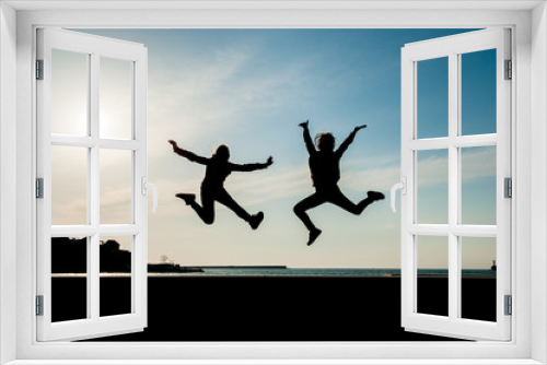 Fototapeta Naklejka Na Ścianę Okno 3D - two happy jumping teen girls on blue sky background at sea sunset