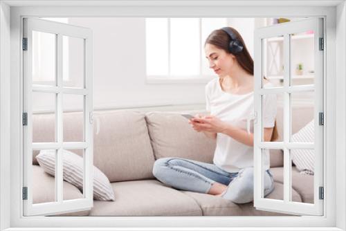 Young woman with cell phone and headphones on beige couch